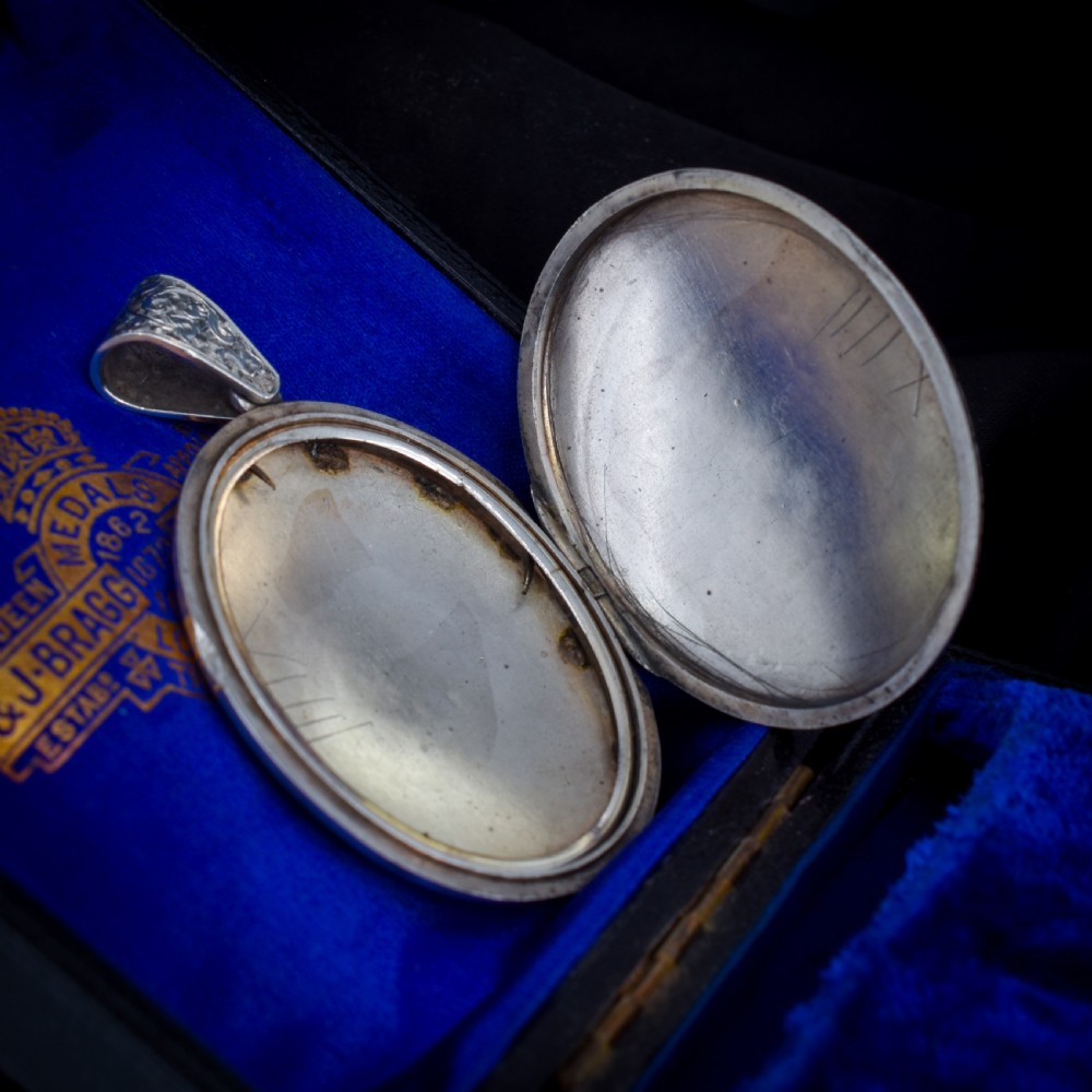 An oval sterling silver locket featuring elaborate hand-engraved scrollwork and a decorative foliage bail. View V