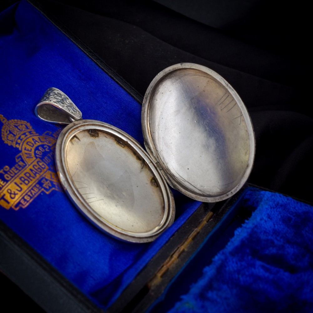 An oval sterling silver locket featuring elaborate hand-engraved scrollwork and a decorative foliage bail. View VI
