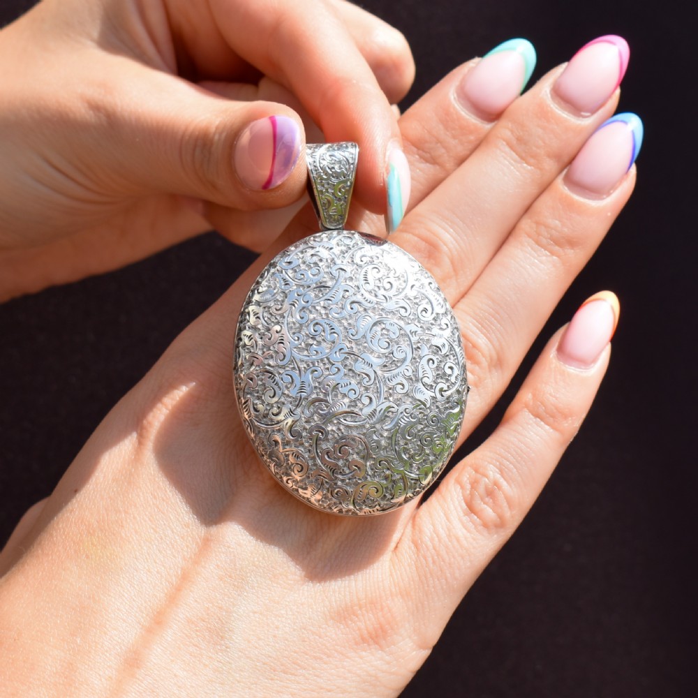 An oval sterling silver locket featuring elaborate hand-engraved scrollwork and a decorative foliage bail. View VII