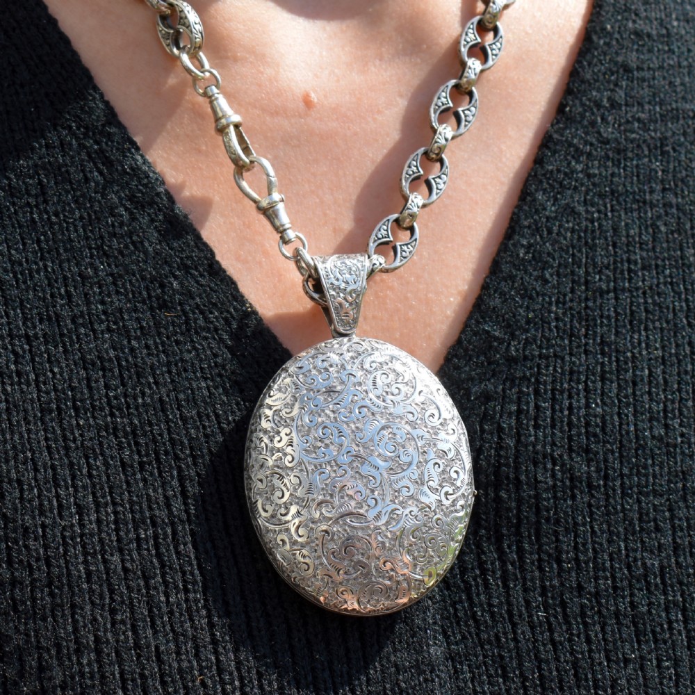 An oval sterling silver locket featuring elaborate hand-engraved scrollwork and a decorative foliage bail. View VIII