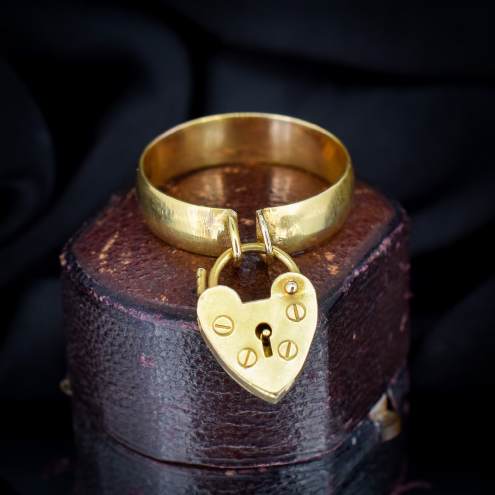 An antique 9ct yellow gold band ring featuring a suspended heart-shaped padlock charm with keyhole and screw head details.