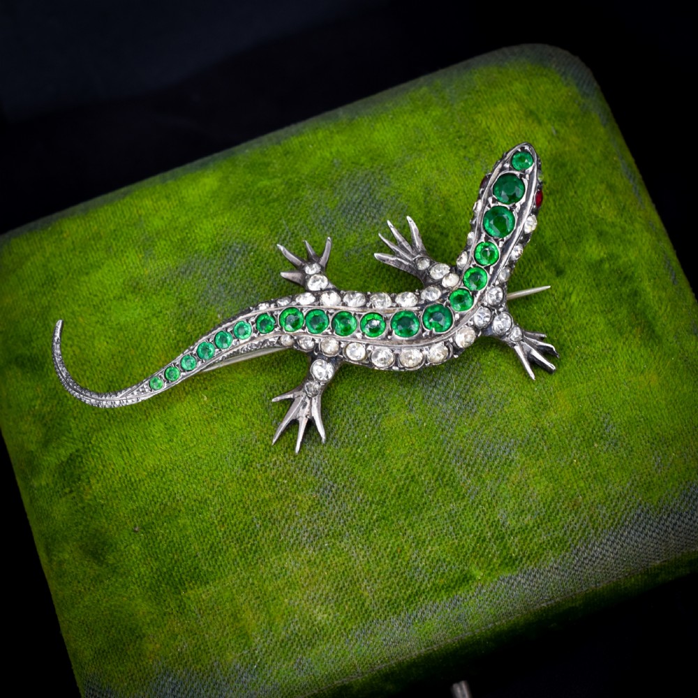 An antique Victorian silver lizard brooch set with a row of green paste stones along the spine and clear paste stones along the outer body. View II