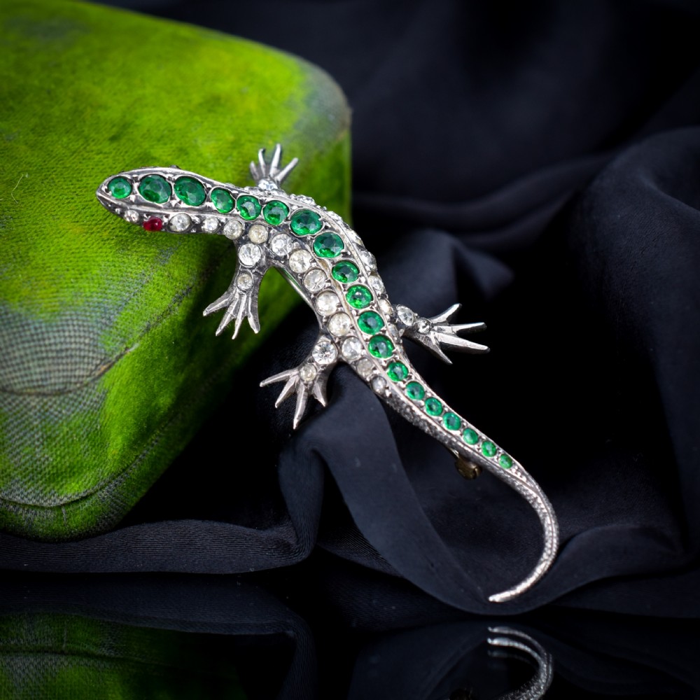 An antique Victorian silver lizard brooch set with a row of green paste stones along the spine and clear paste stones along the outer body. View IV