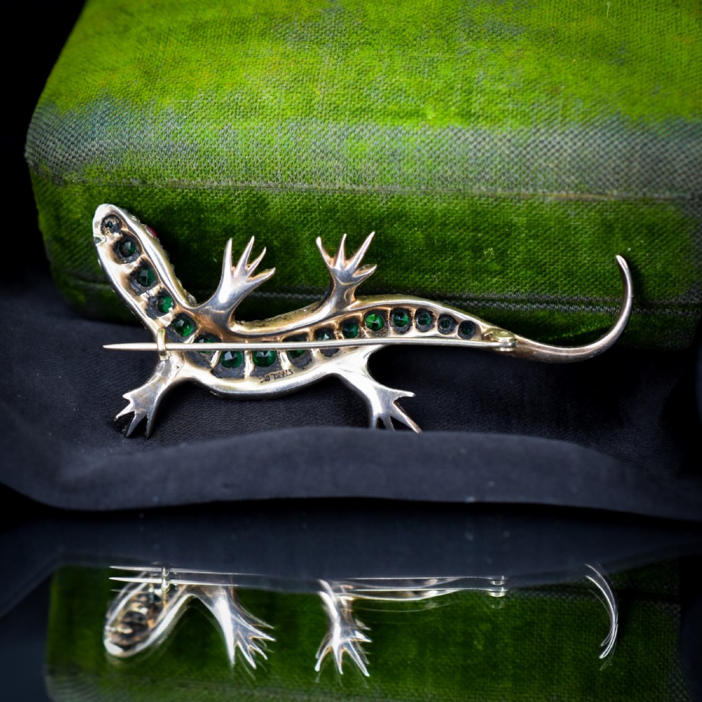 An antique Victorian silver lizard brooch set with a row of green paste stones along the spine and clear paste stones along the outer body. View V