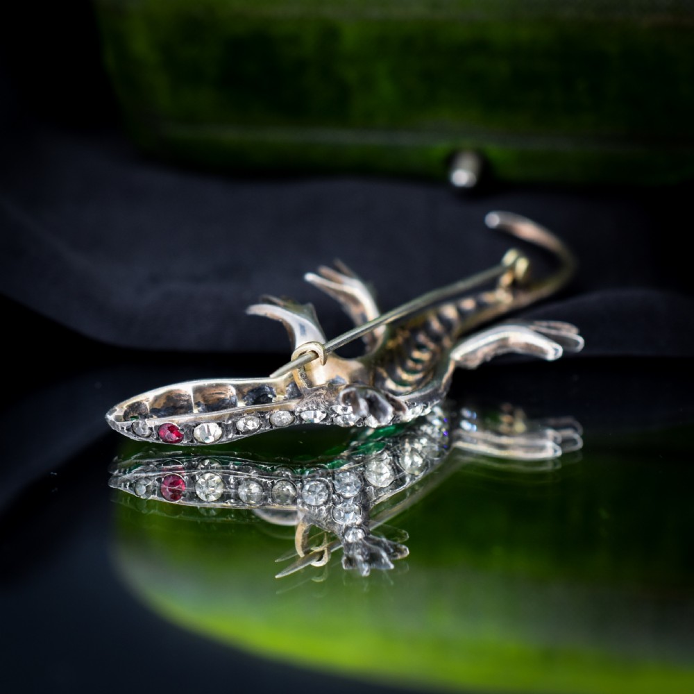 An antique Victorian silver lizard brooch set with a row of green paste stones along the spine and clear paste stones along the outer body. View VI
