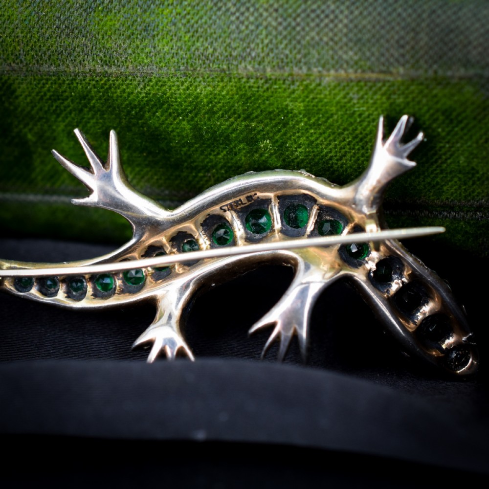 An antique Victorian silver lizard brooch set with a row of green paste stones along the spine and clear paste stones along the outer body. View VII