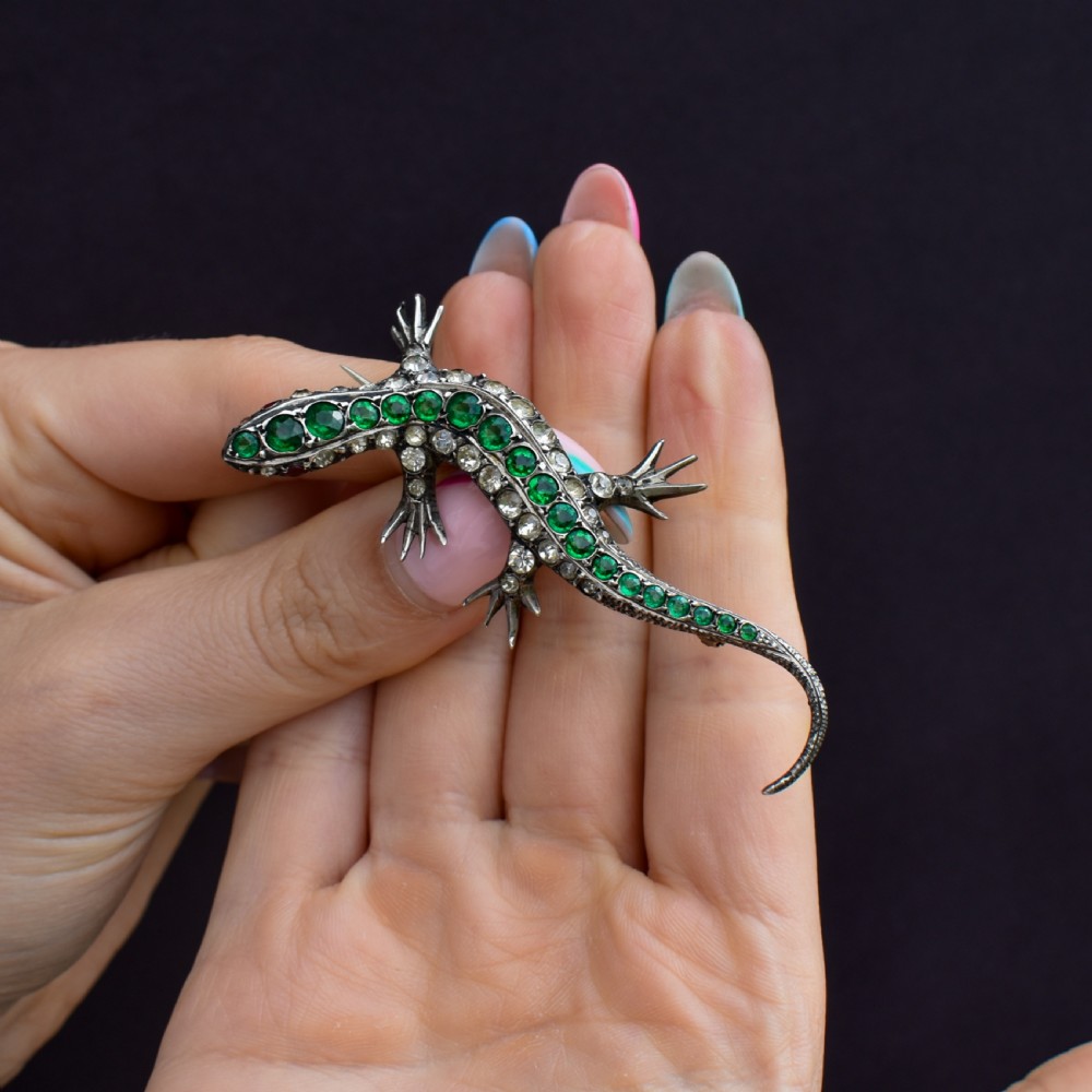 An antique Victorian silver lizard brooch set with a row of green paste stones along the spine and clear paste stones along the outer body. View IX