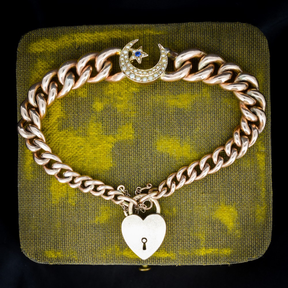 An antique 9ct rose gold curb chain bracelet featuring a heart padlock clasp and a central crescent moon and star motif set with seed pearls.