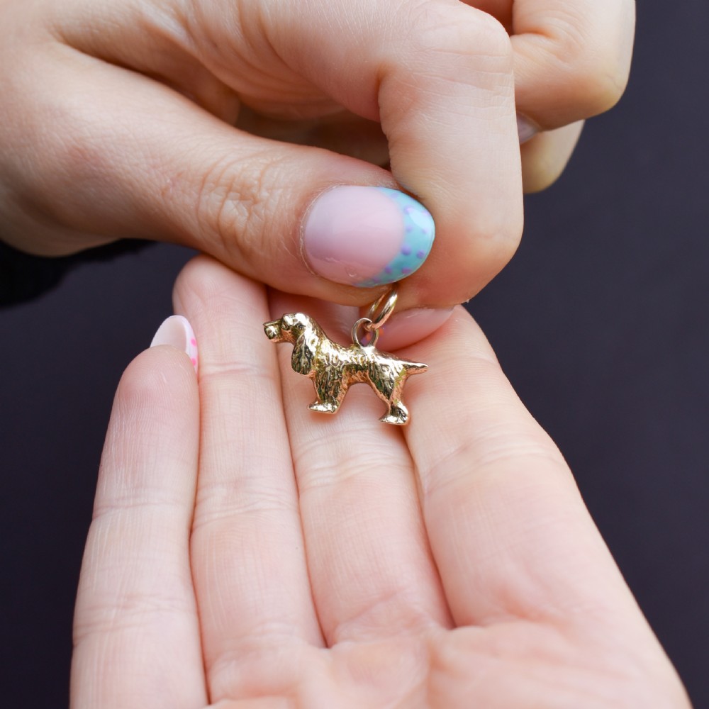 A small 9ct yellow gold charm cast in the detailed shape of a standing spaniel dog with a textured coat and an attached jump ring.