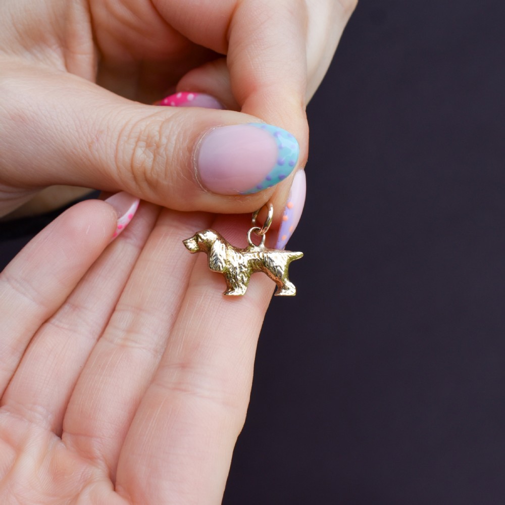 A small 9ct yellow gold charm cast in the detailed shape of a standing spaniel dog with a textured coat and an attached jump ring. View II