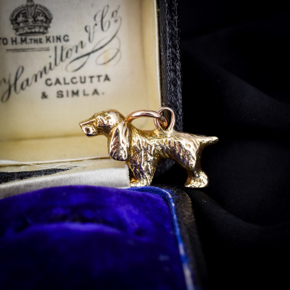 A small 9ct yellow gold charm cast in the detailed shape of a standing spaniel dog with a textured coat and an attached jump ring. View IV
