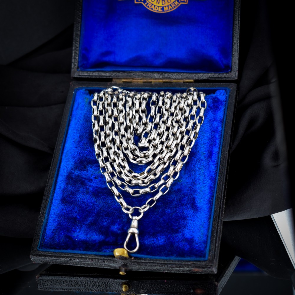 An antique silver long guard chain with belcher links coiled neatly inside a royal blue velvet presentation box fitted with a dog clip clasp.