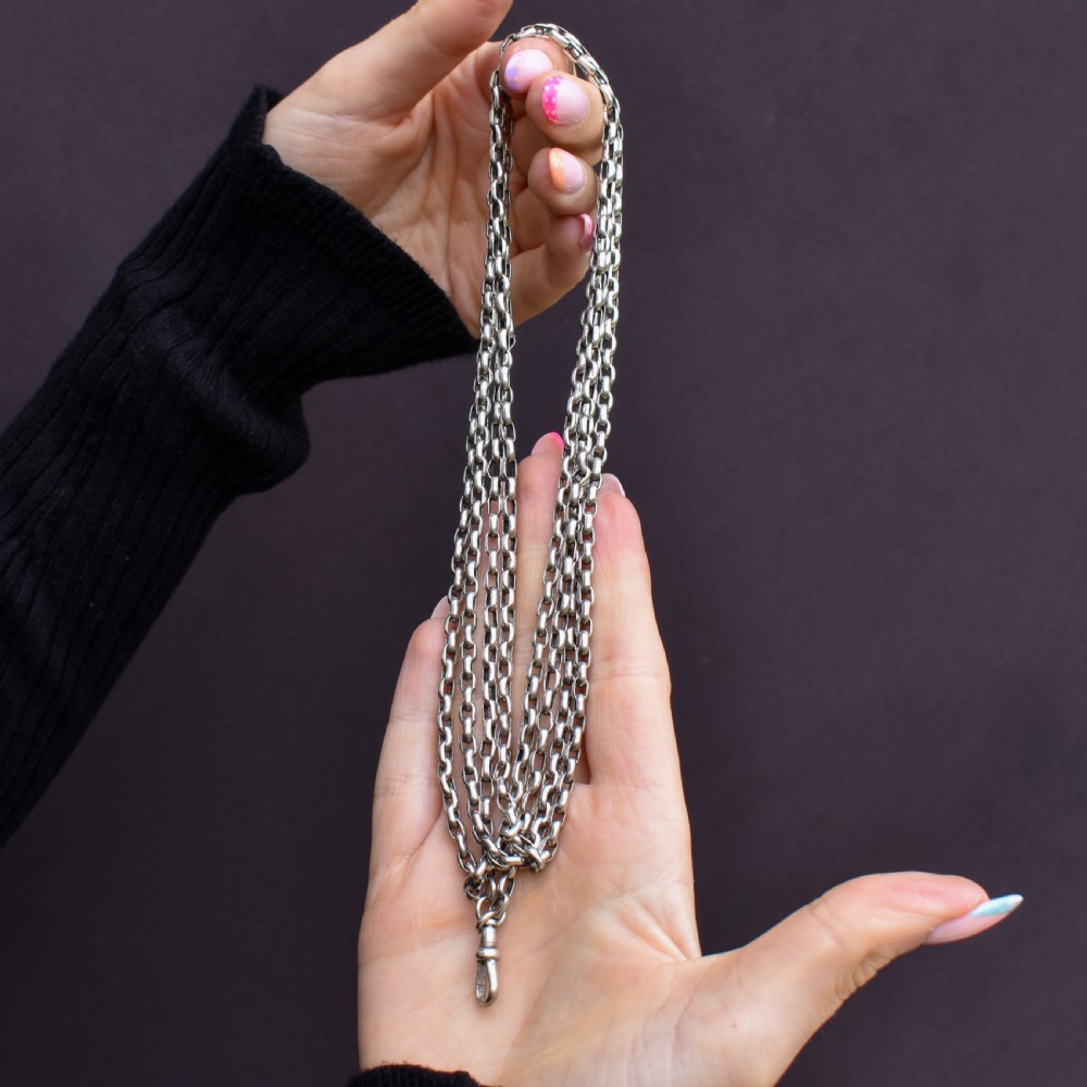 An antique silver long guard chain with belcher links coiled neatly inside a royal blue velvet presentation box fitted with a dog clip clasp. View X