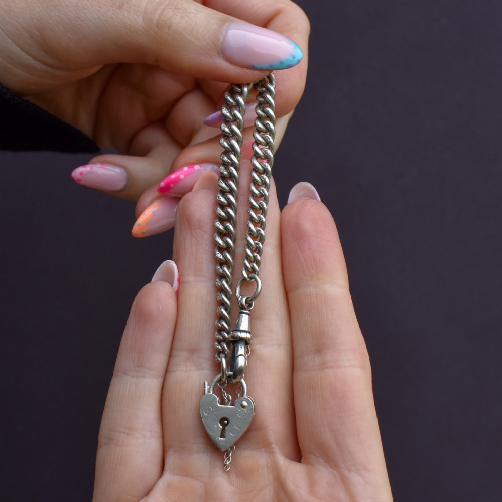An antique sterling silver graduated curb link bracelet featuring a heart-shaped padlock clasp, safety chain, and a swivel dog clip attachment. View X