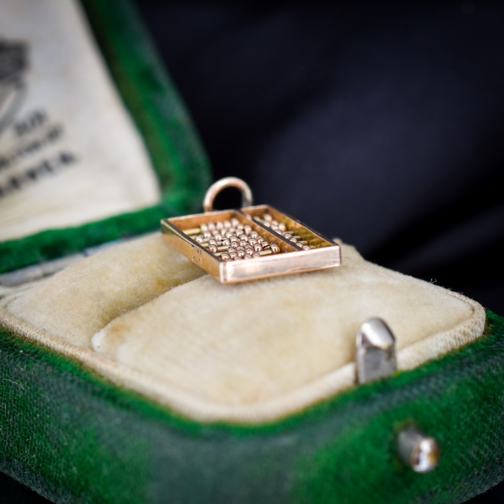 A miniature rectangular 14ct yellow gold abacus charm featuring multiple rows of small gold beads framed with a top suspension ring. View II