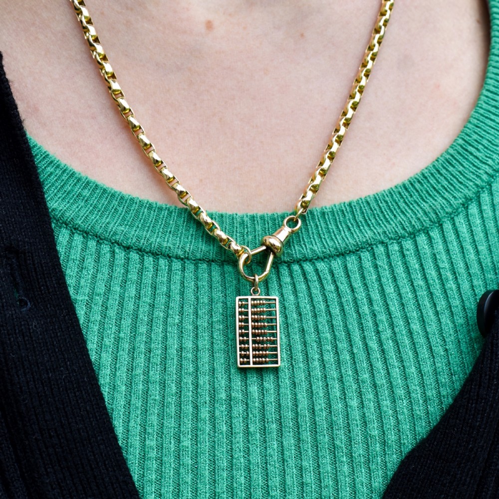 A miniature rectangular 14ct yellow gold abacus charm featuring multiple rows of small gold beads framed with a top suspension ring. View VII
