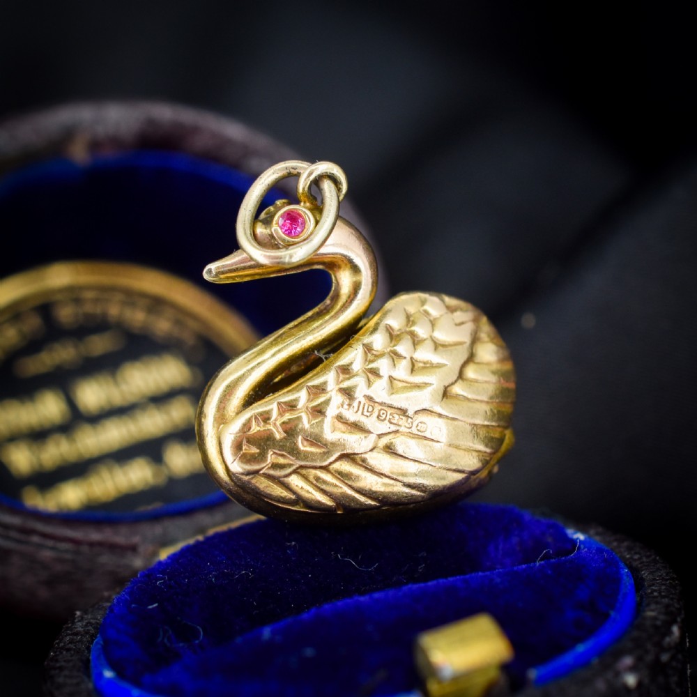 A small 9ct yellow gold swan charm featuring textured feather details, a round ruby set as the eye, and visible hallmarks stamped on the side.