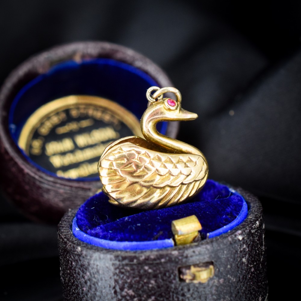 A small 9ct yellow gold swan charm featuring textured feather details, a round ruby set as the eye, and visible hallmarks stamped on the side. View III