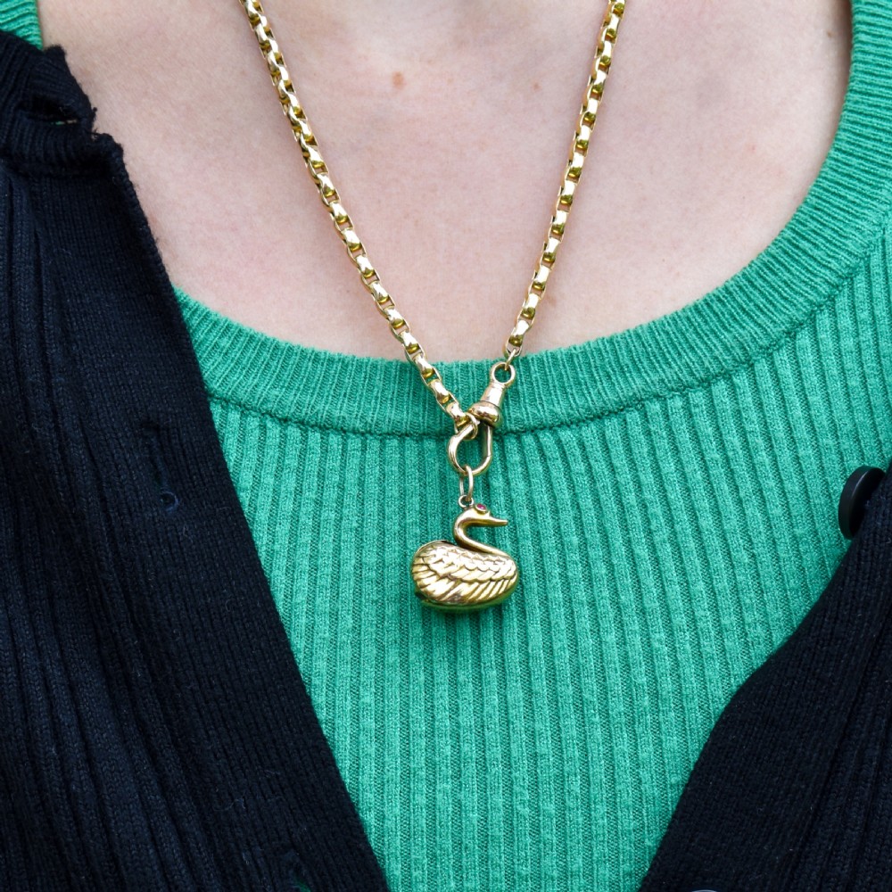 A small 9ct yellow gold swan charm featuring textured feather details, a round ruby set as the eye, and visible hallmarks stamped on the side. View VIII