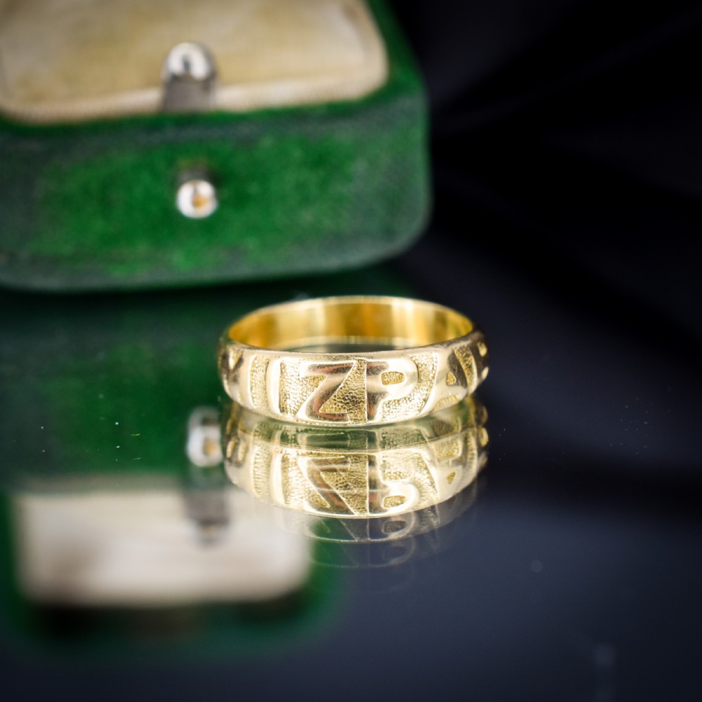 An antique 18ct yellow gold band ring featuring the word MIZPAH in raised capital lettering against a stippled textured background. View II