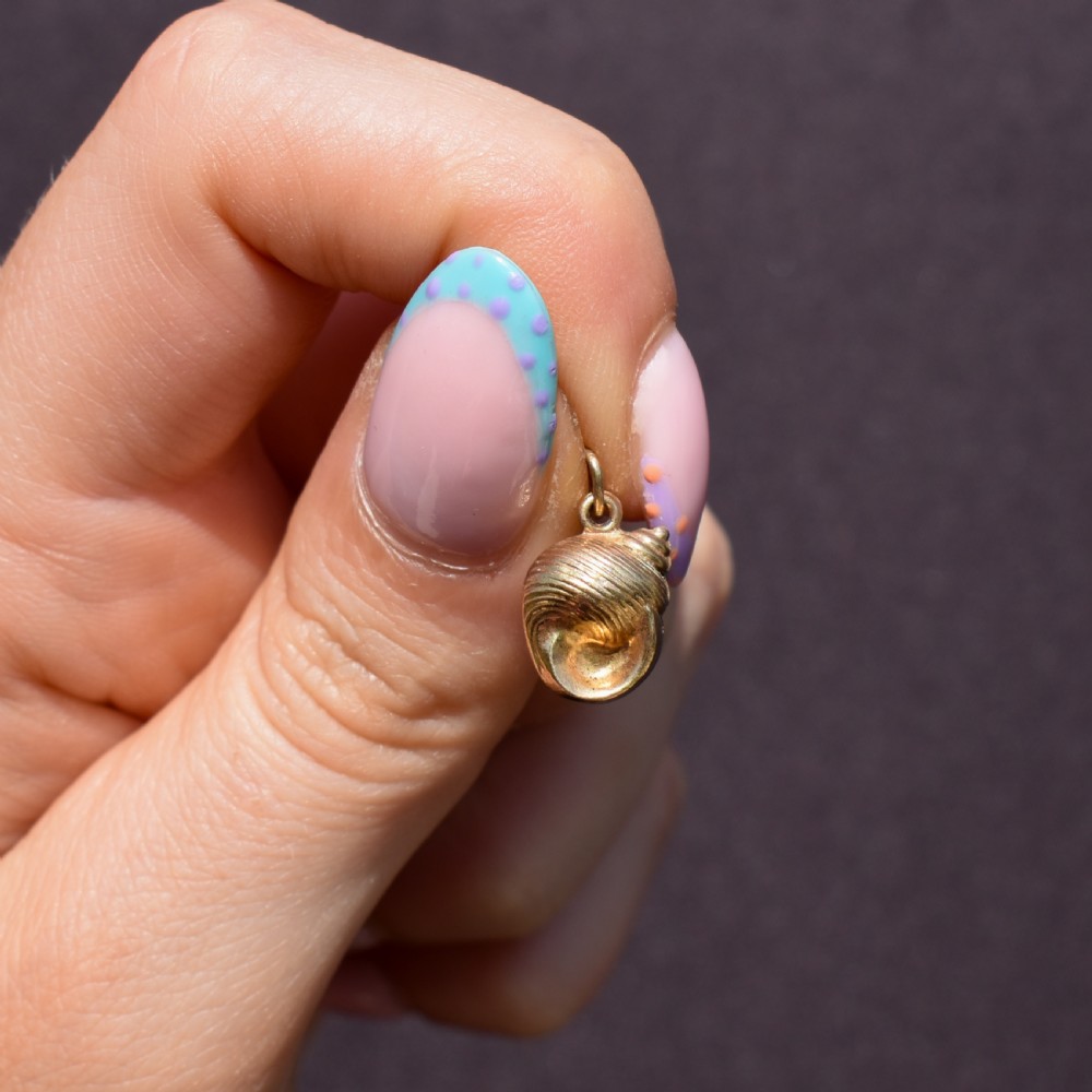 A small three-dimensional 9ct yellow gold seashell charm with ribbed texturing and a top suspension ring. View II