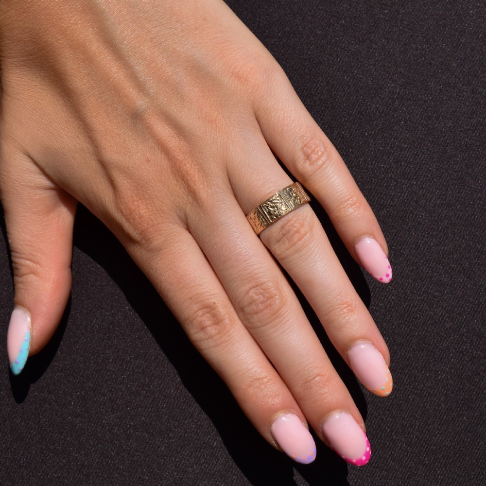 A wide 9ct yellow gold Victorian cigar band ring displaying carved square floral panels around the circumference. View V