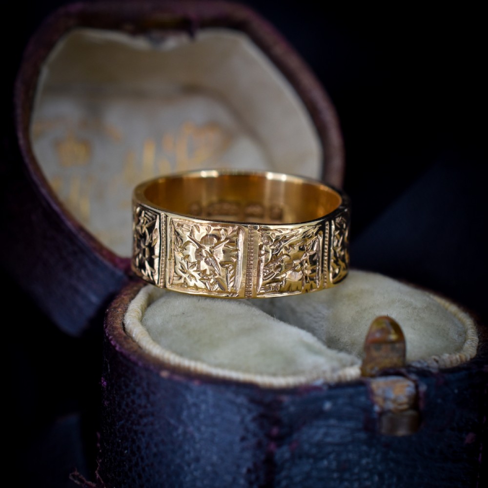 A wide 9ct yellow gold Victorian cigar band ring displaying carved square floral panels around the circumference. View IX