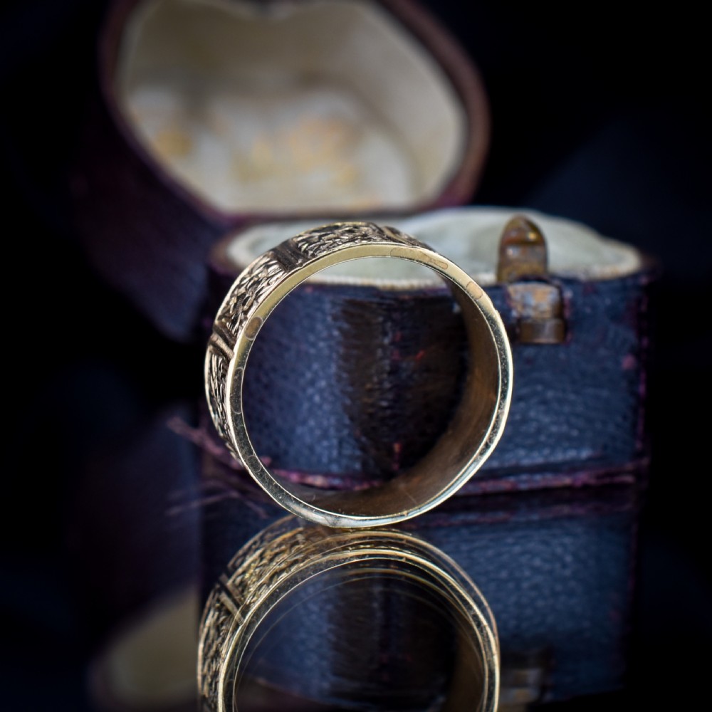 A wide 9ct yellow gold Victorian cigar band ring displaying carved square floral panels around the circumference. View X