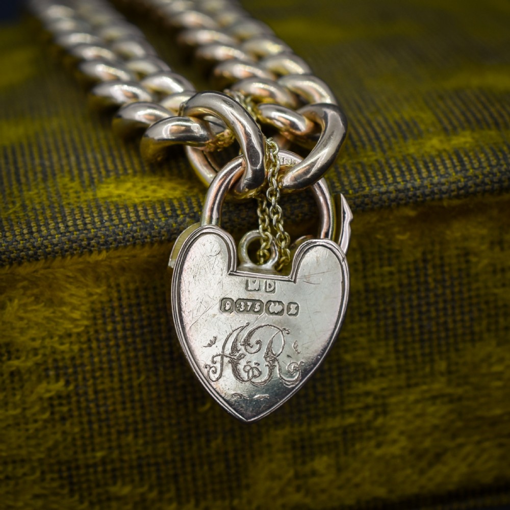 A 9ct yellow gold curb link chain bracelet featuring alternating plain and hand-engraved links, fitted with an engraved heart-shaped padlock clasp and safety chain. View IV