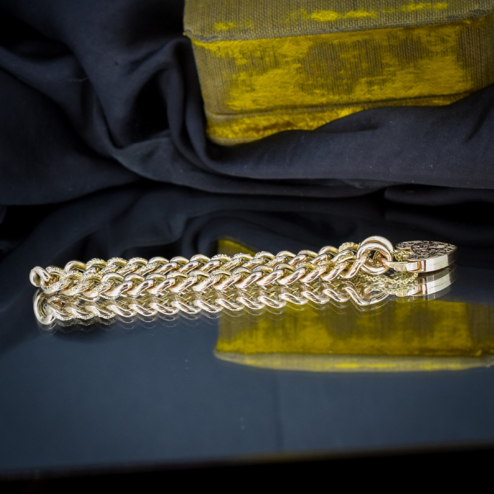 A 9ct yellow gold curb link chain bracelet featuring alternating plain and hand-engraved links, fitted with an engraved heart-shaped padlock clasp and safety chain. View V