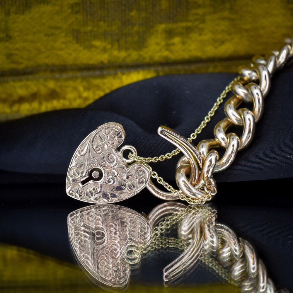 A 9ct yellow gold curb link chain bracelet featuring alternating plain and hand-engraved links, fitted with an engraved heart-shaped padlock clasp and safety chain. View VII