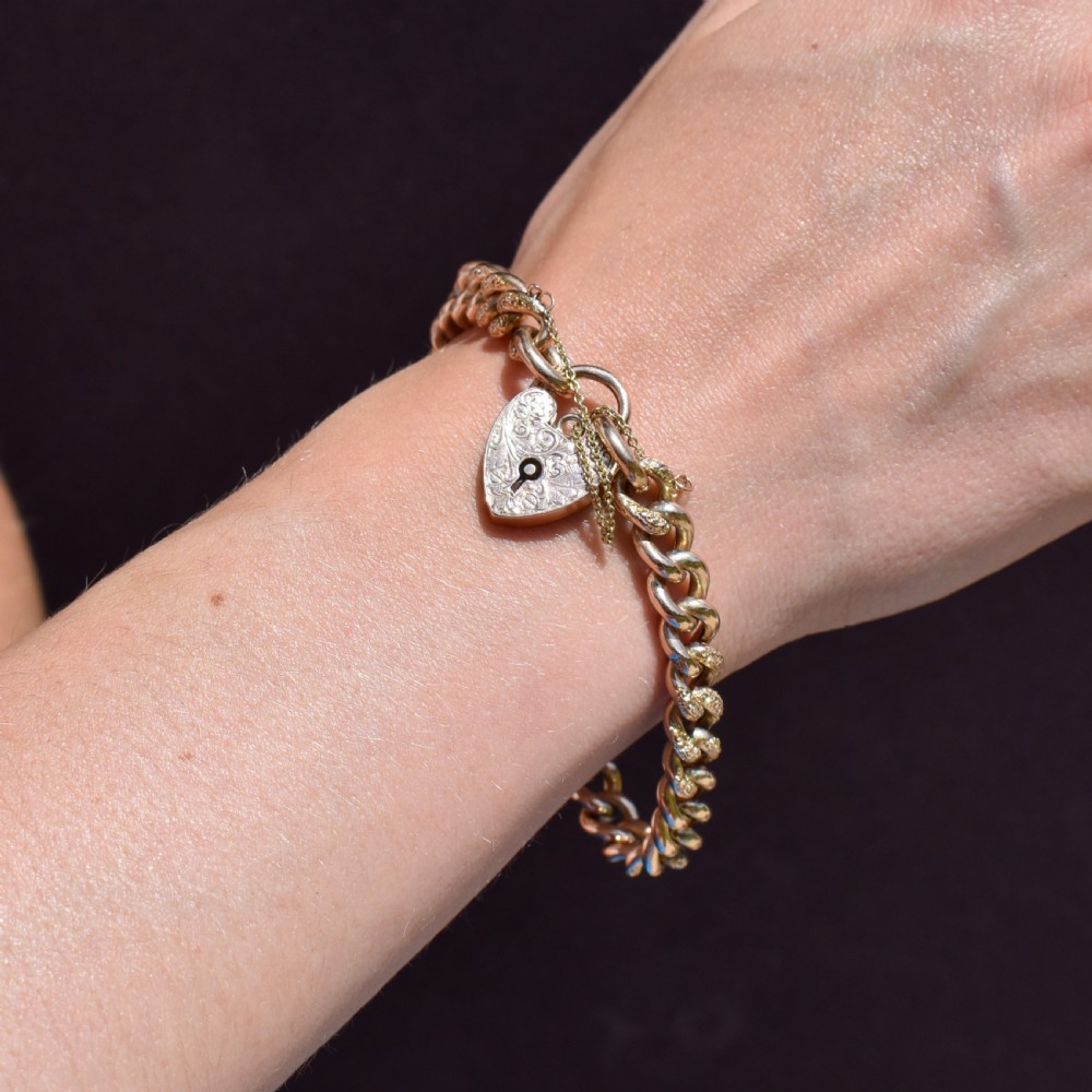 A 9ct yellow gold curb link chain bracelet featuring alternating plain and hand-engraved links, fitted with an engraved heart-shaped padlock clasp and safety chain. View VIII