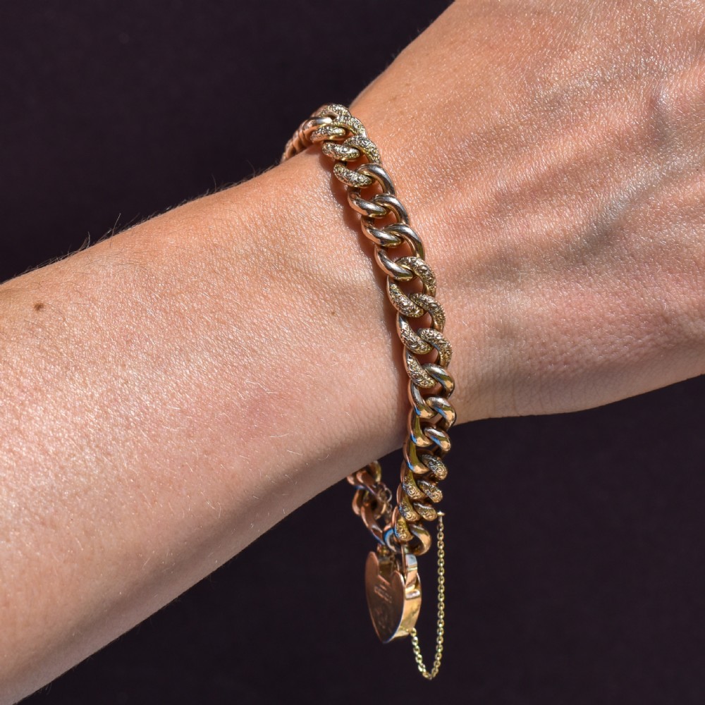 A 9ct yellow gold curb link chain bracelet featuring alternating plain and hand-engraved links, fitted with an engraved heart-shaped padlock clasp and safety chain. View IX