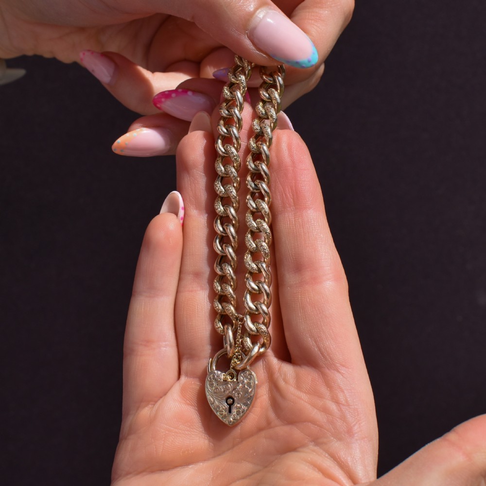 A 9ct yellow gold curb link chain bracelet featuring alternating plain and hand-engraved links, fitted with an engraved heart-shaped padlock clasp and safety chain. View X