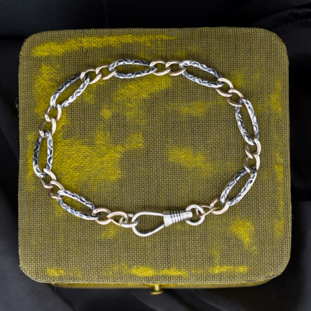 An antique chain bracelet consisting of patterned niello silver links connected by smooth gold links and secured with a swivel dog clip clasp.