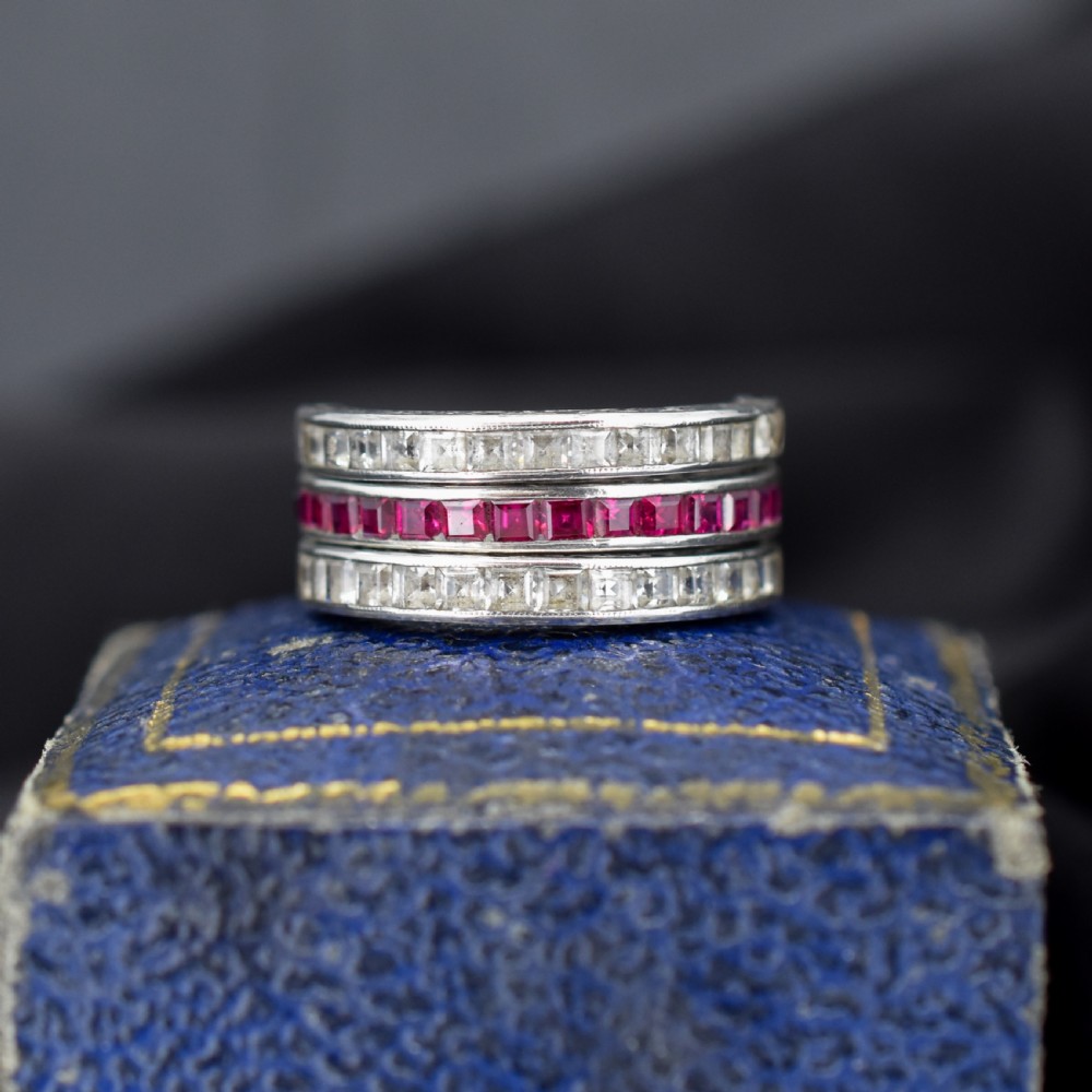 An Art Deco sterling silver swivel eternity ring featuring a central band of channel-set red paste stones flanked by hinged swivelling bands of clear paste stones.