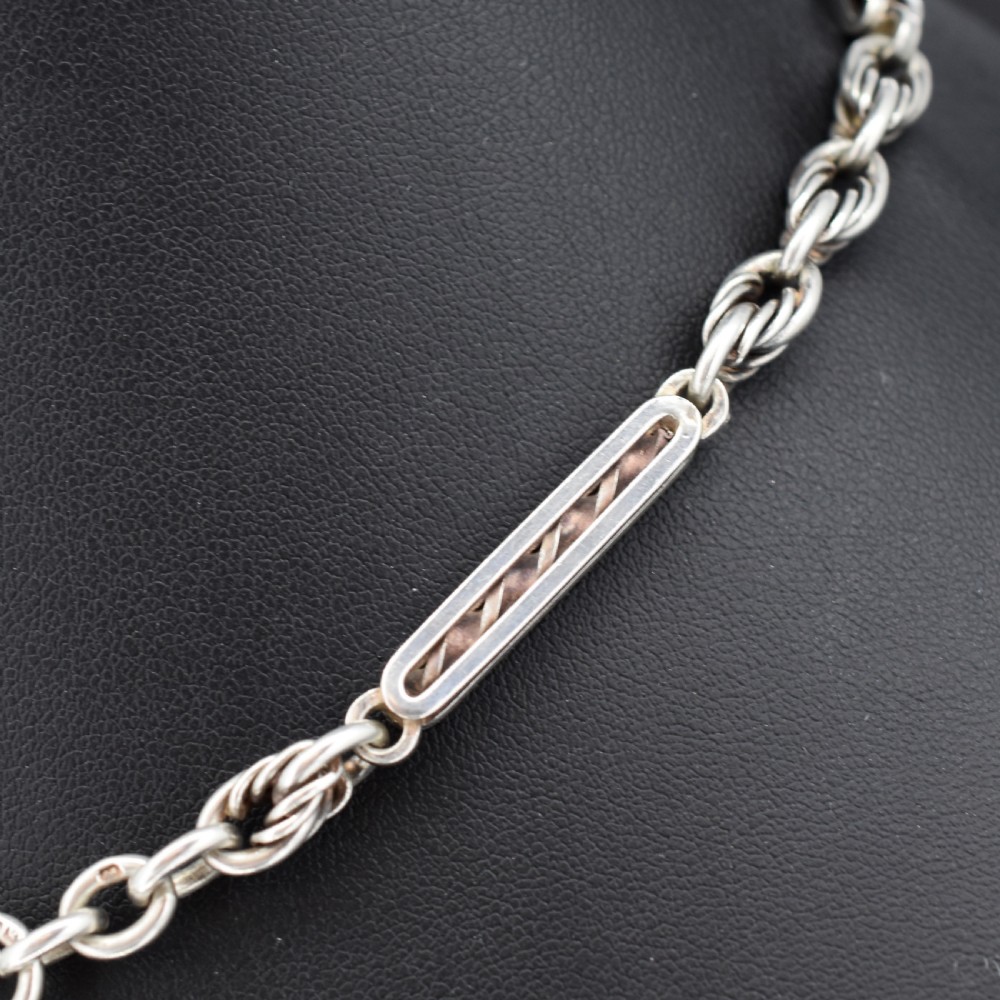 An antique sterling silver Albert chain necklace featuring elongated bar links, twisted rope sections, a T-bar attachment, and a swivel clasp. View V