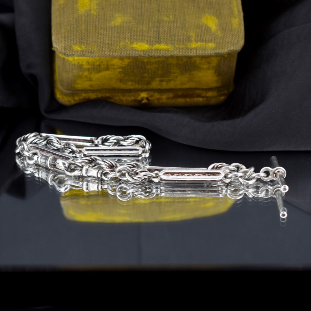 An antique sterling silver Albert chain necklace featuring elongated bar links, twisted rope sections, a T-bar attachment, and a swivel clasp. View VII