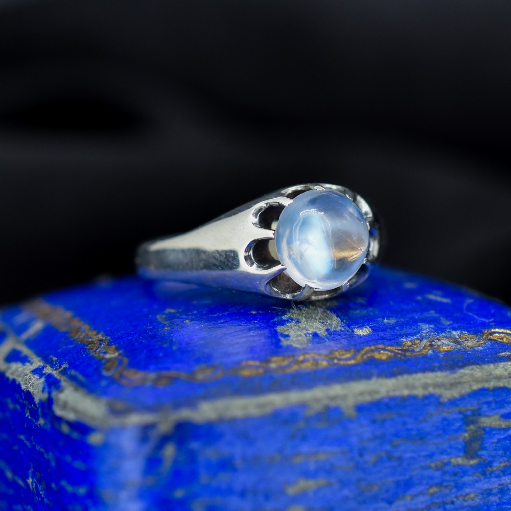 An antique sterling silver ring featuring a smooth oval moonstone cabochon held within pierced, decorative silver shoulders.