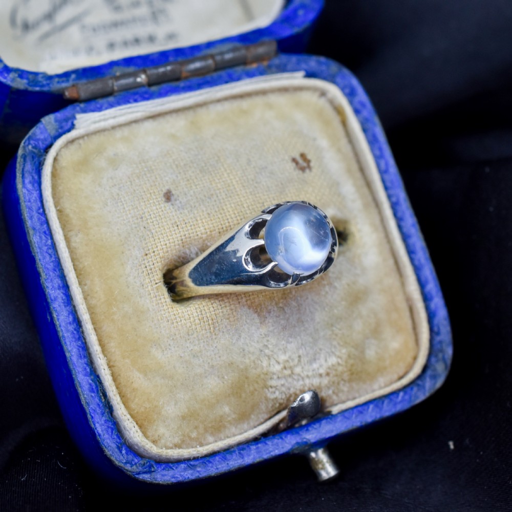 An antique sterling silver ring featuring a smooth oval moonstone cabochon held within pierced, decorative silver shoulders. View II