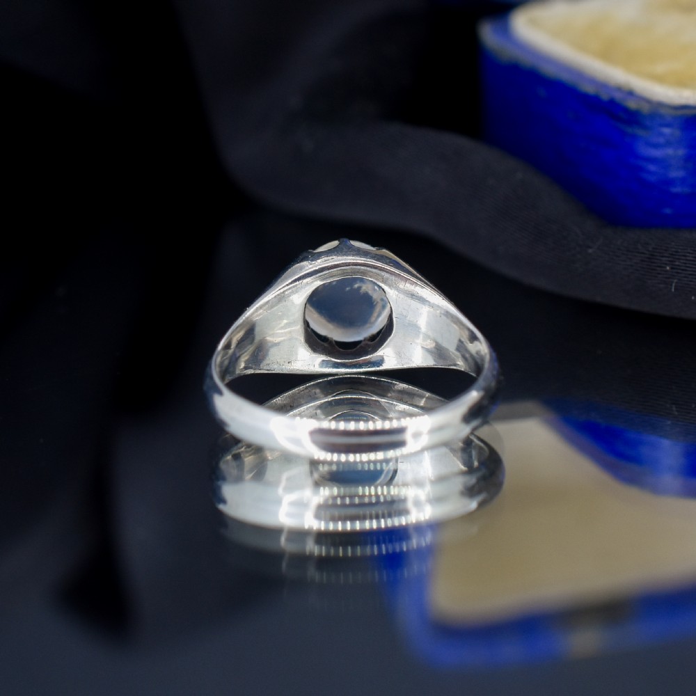 An antique sterling silver ring featuring a smooth oval moonstone cabochon held within pierced, decorative silver shoulders. View IV