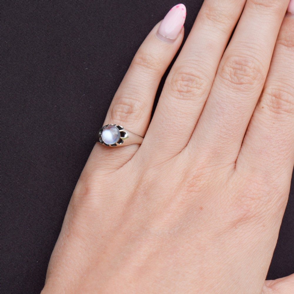 An antique sterling silver ring featuring a smooth oval moonstone cabochon held within pierced, decorative silver shoulders. View VI