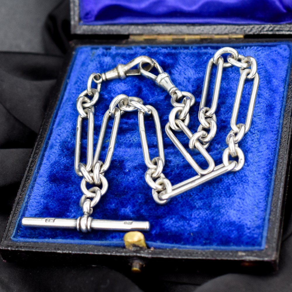 An antique sterling silver trombone link pocket watch chain with a T-bar attachment and dog clip fastener.