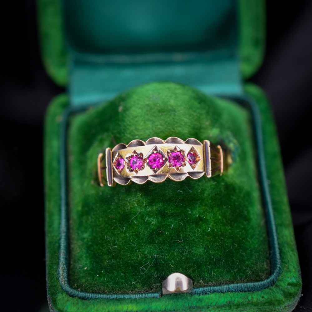 An antique Victorian 15ct yellow gold band ring set with five red-pink rubies in star-engraved settings with a scalloped border.