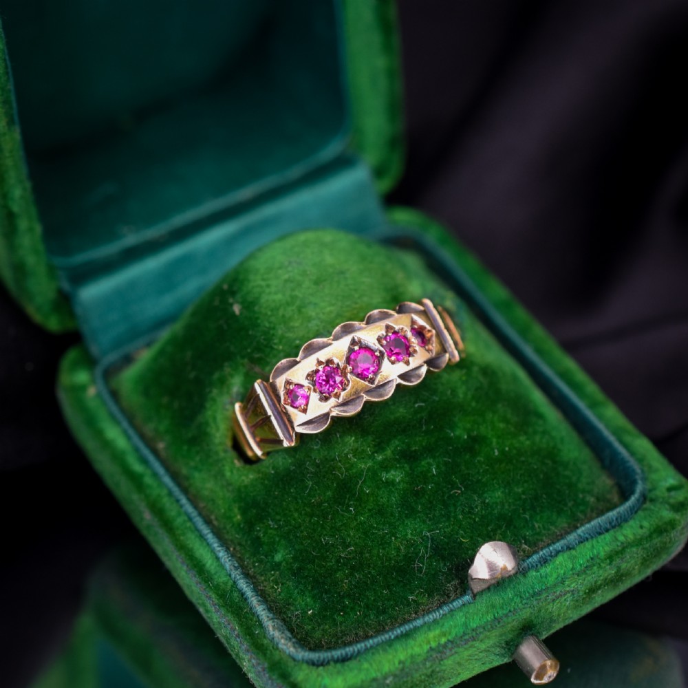 An antique Victorian 15ct yellow gold band ring set with five red-pink rubies in star-engraved settings with a scalloped border. View II