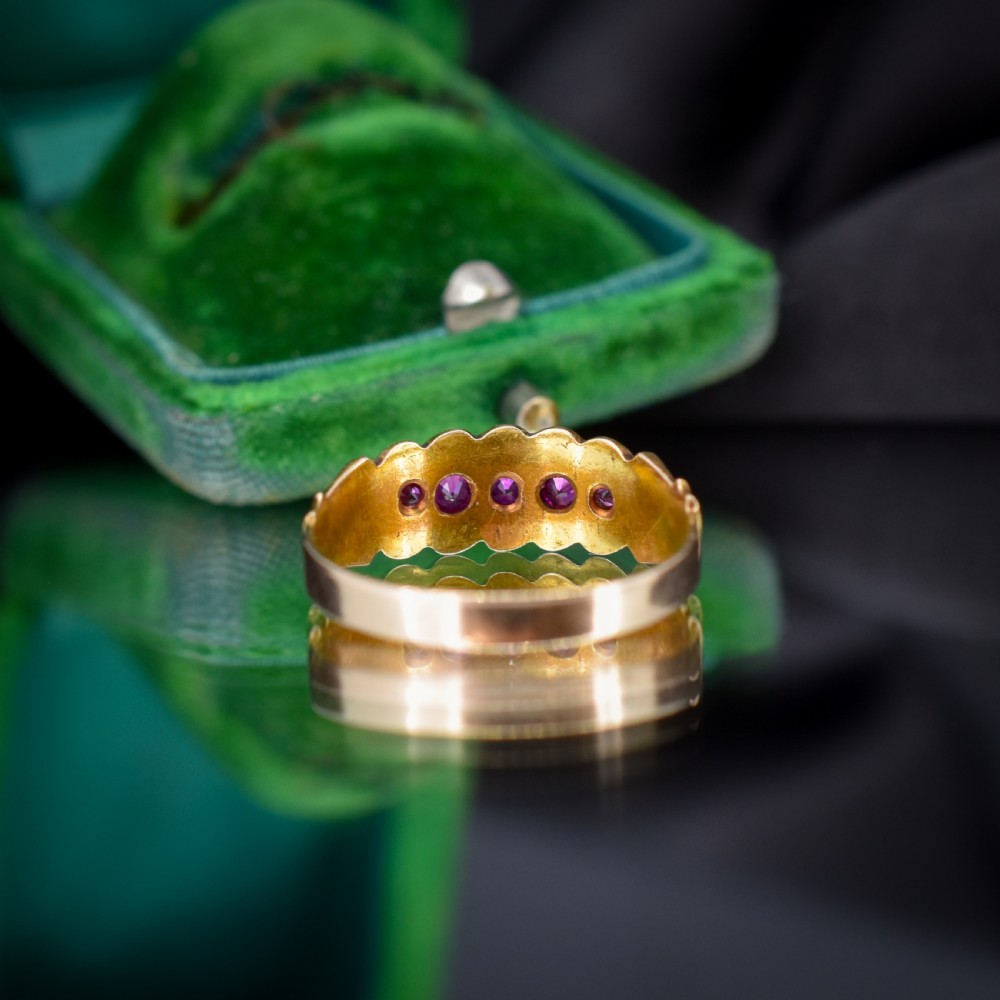 An antique Victorian 15ct yellow gold band ring set with five red-pink rubies in star-engraved settings with a scalloped border. View V