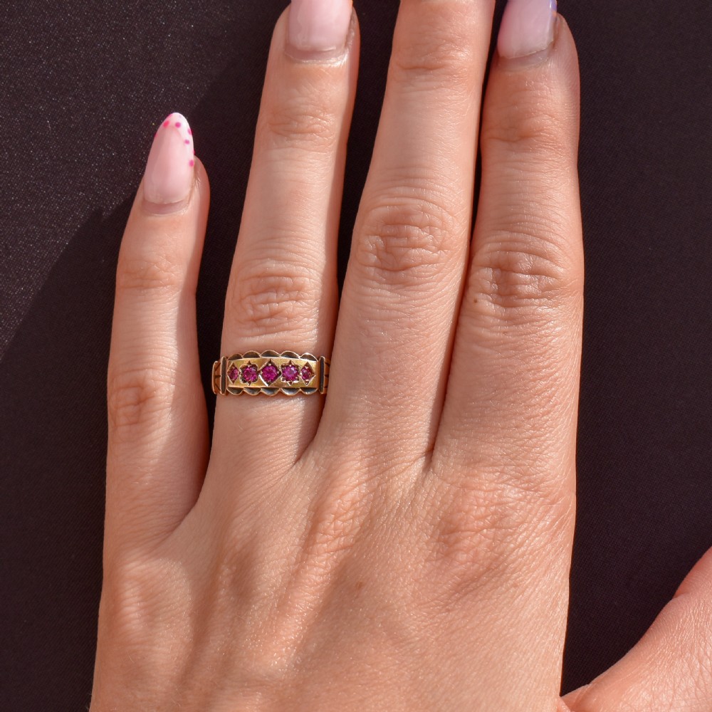 An antique Victorian 15ct yellow gold band ring set with five red-pink rubies in star-engraved settings with a scalloped border. View IX