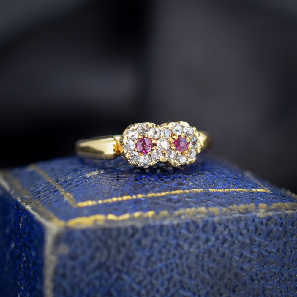 An antique 18ct yellow gold ring featuring a figure-of-eight double cluster set with two central pinkish-red rubies surrounded by small diamonds.