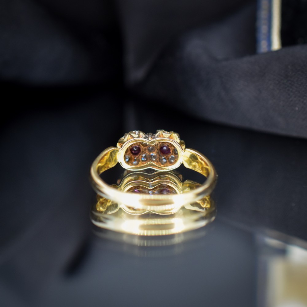 An antique 18ct yellow gold ring featuring a figure-of-eight double cluster set with two central pinkish-red rubies surrounded by small diamonds. View VI