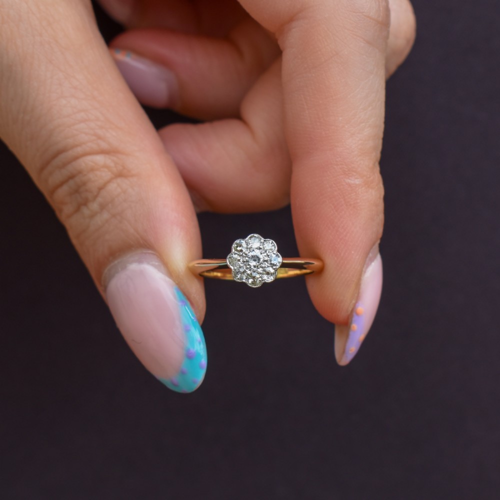 An antique diamond daisy cluster ring set in platinum with an 18ct yellow gold band resting inside an open red heart-shaped velvet box. View II
